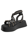 Sandalia de mujer negra de cuero con diseño gladiador y apliques metálicos dorados, estilo casual rockero.